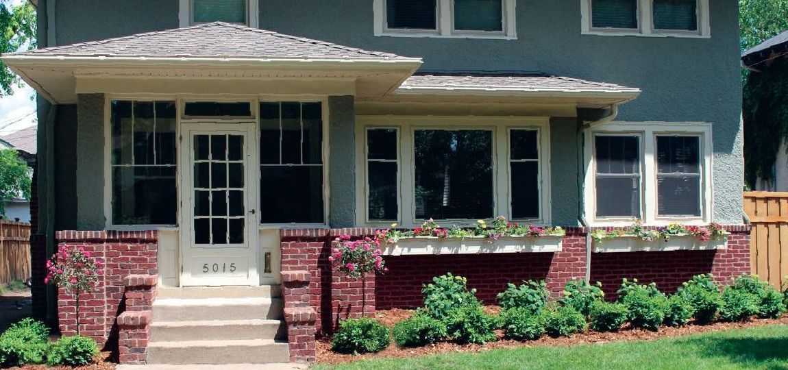 Clean, low-maintenance front yard in Minneapolis with boxwoods, roses, a tree, and flower-filled window boxes