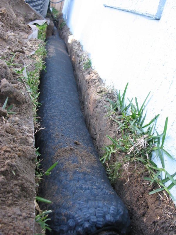 A large tire is laying in the dirt next to a wall.