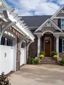 White house with a pergola over a garage and a brick facade entrance.