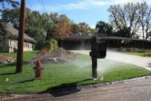 A sprinkler waters a green lawn in front of a house, with a red fire hydrant in view.