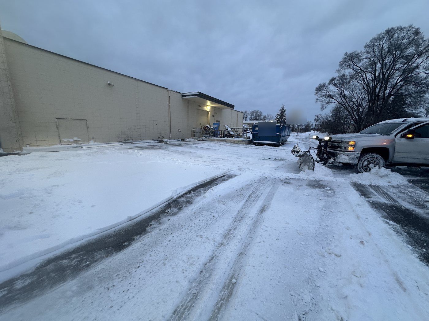 Pickup truck with a snow plow clearing a warehouse parking lot at dawn