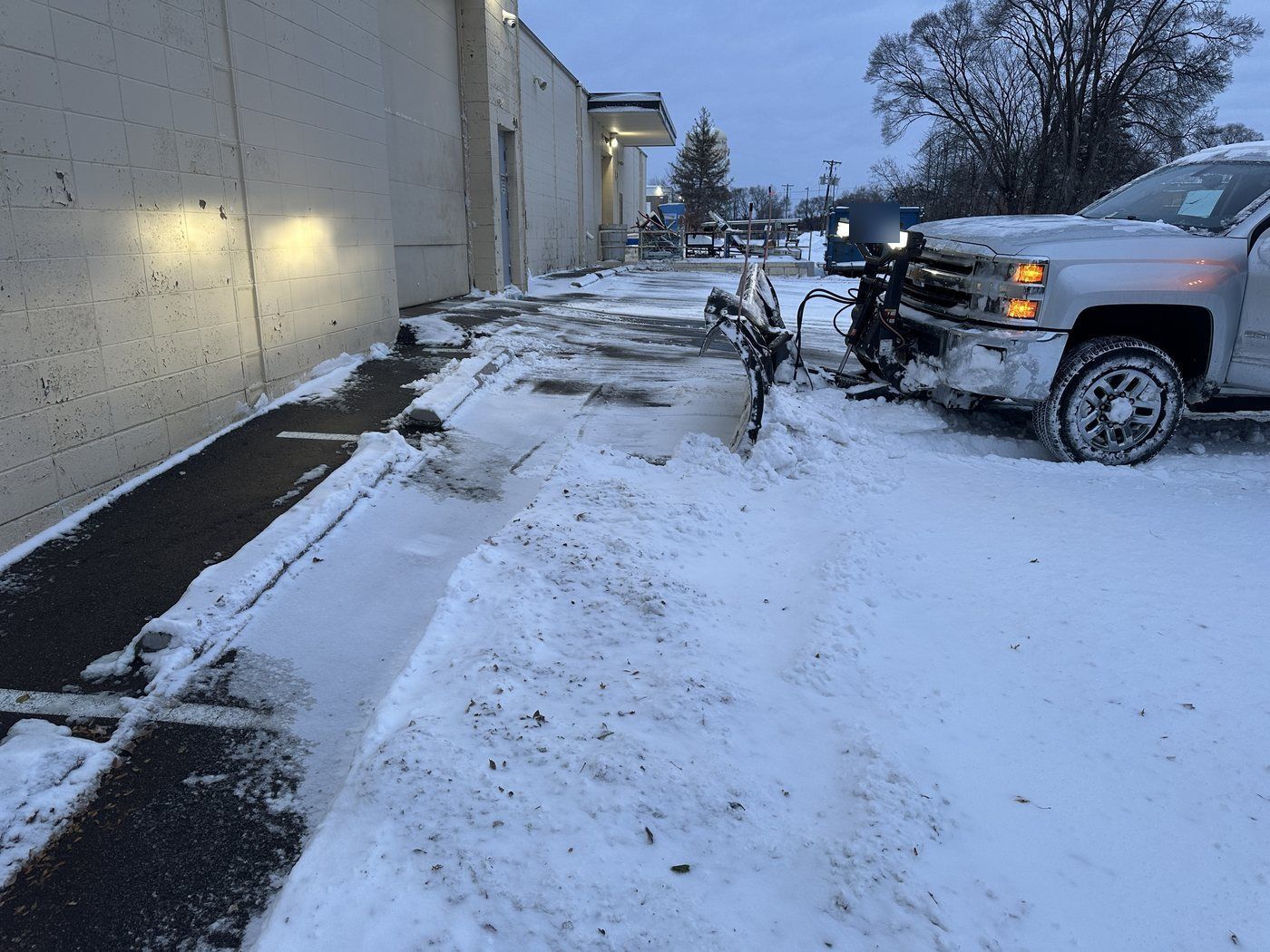 Snow plow clearing the drive along a warehouse wall beside a cleared strip of pavement