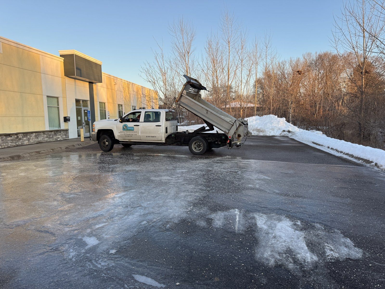 KG Landscape truck with a salt spreader treating a cleared commercial parking lot