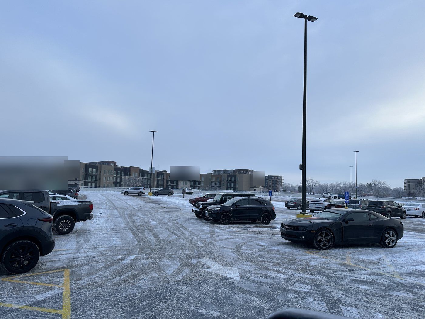 Plowed parking lot with parked cars and light snow in the tire tracks