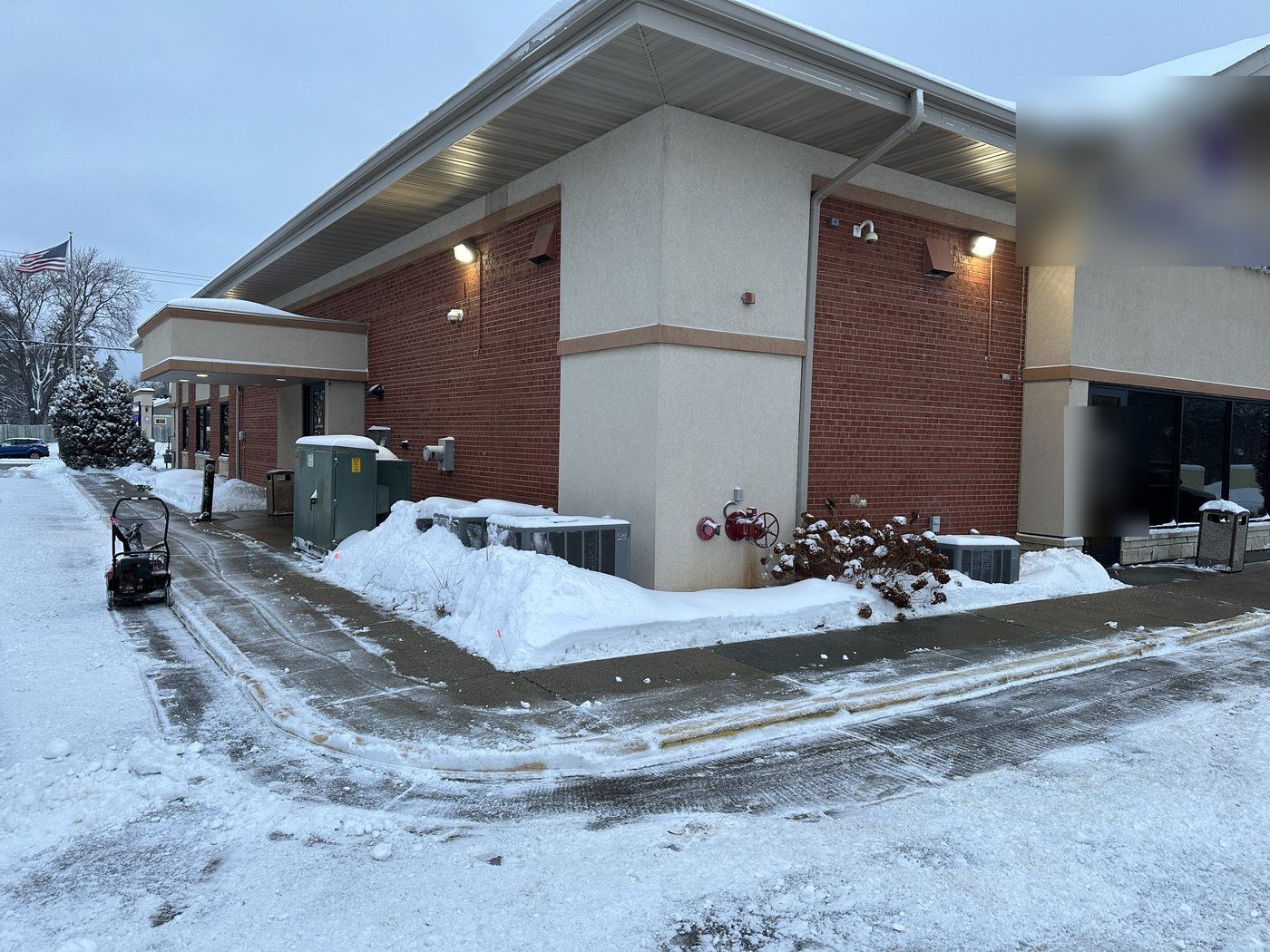 Cleared walk at the corner of a commercial building with a snowblower nearby