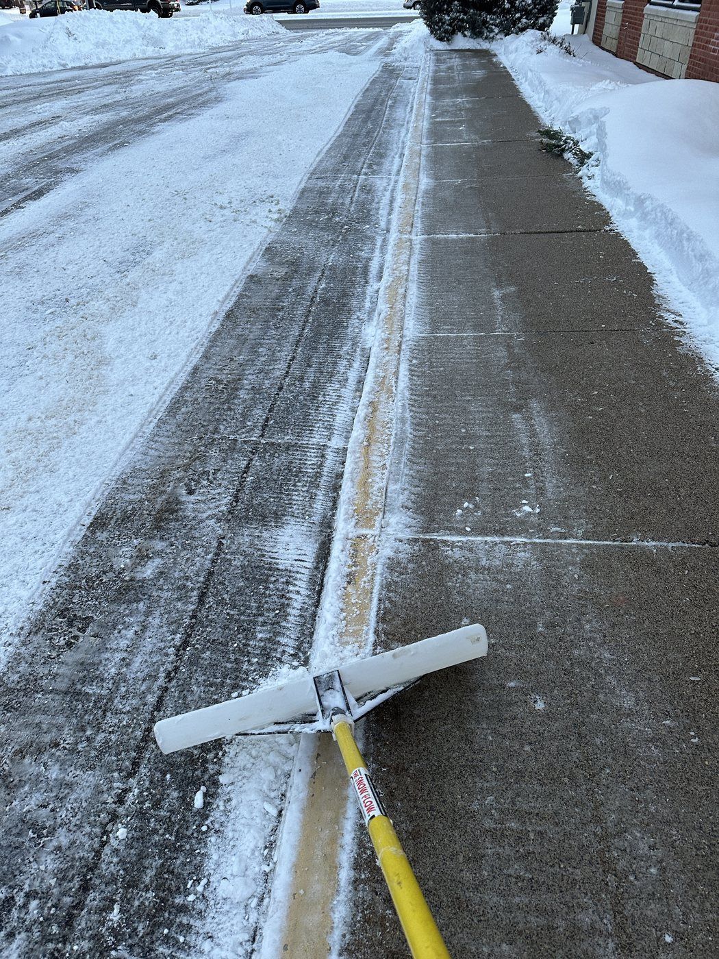 Hand scraper taking the last layer of snow off a cleared concrete walk