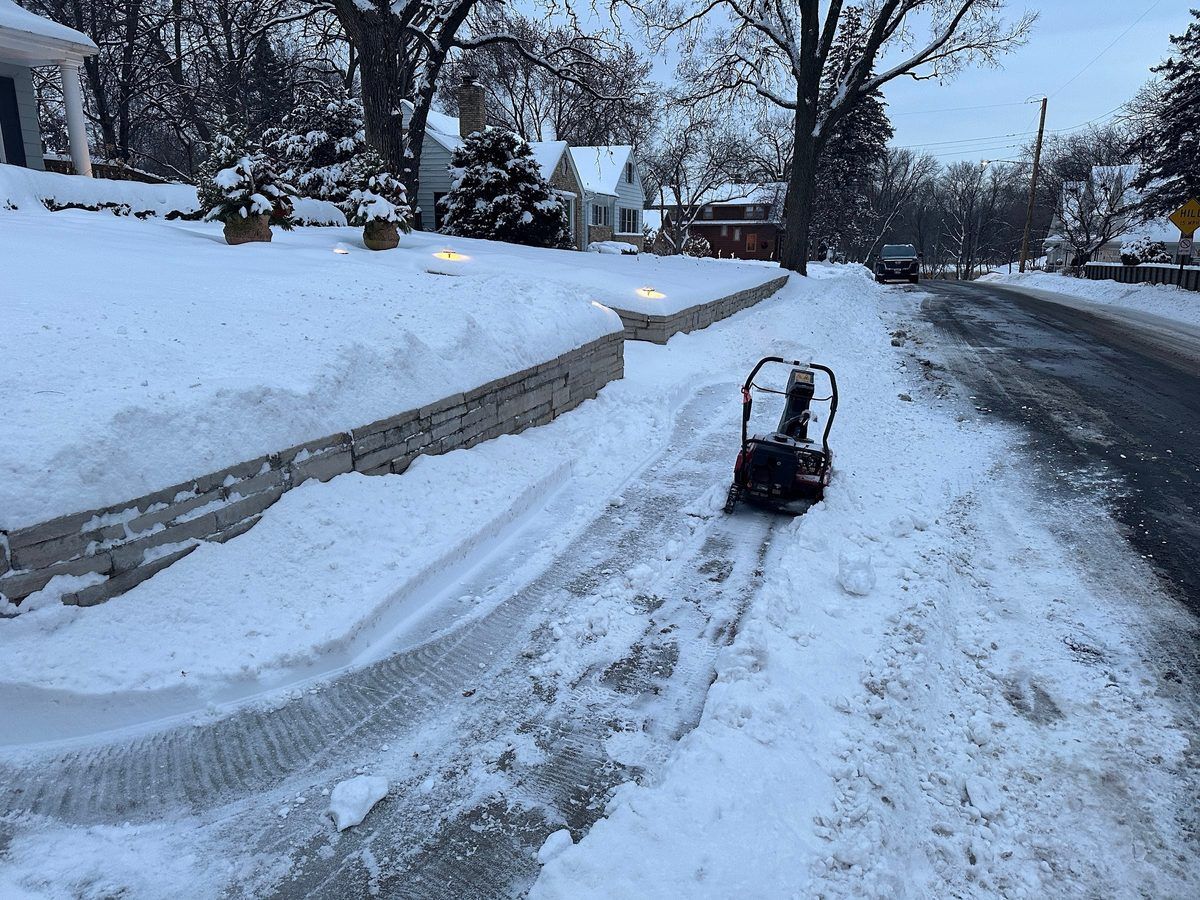 Snow blower clearing a sidewalk beside a plowed street