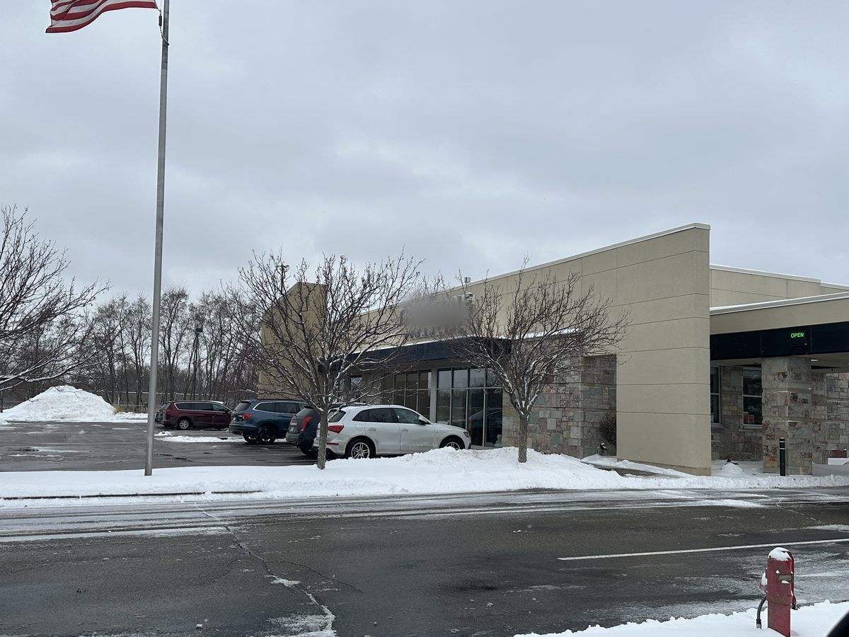 Commercial building with a flagpole and parked cars beside a plowed street