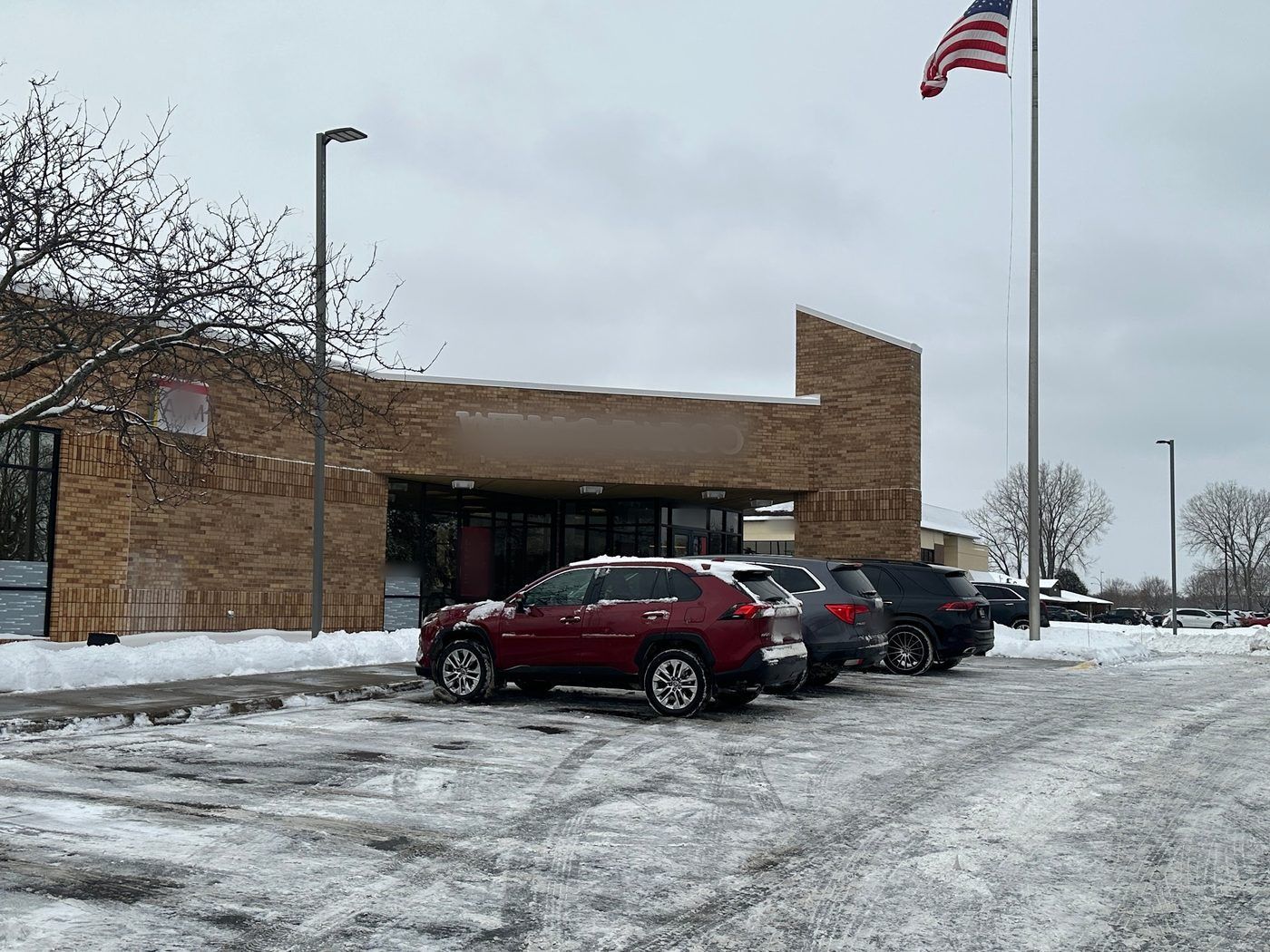 Plowed parking lot with cars beside a brick commercial building