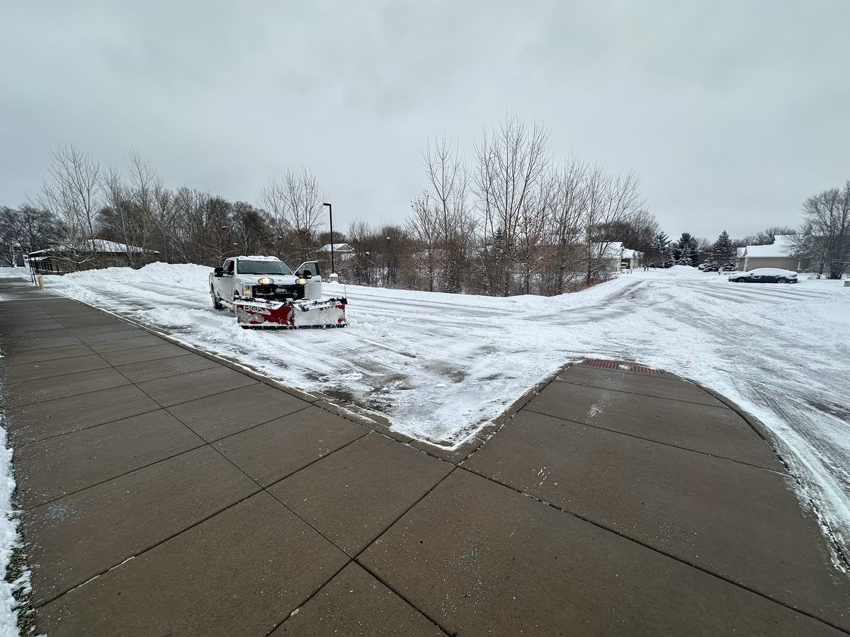 Cleared concrete sidewalk with a plow truck working the lot behind it