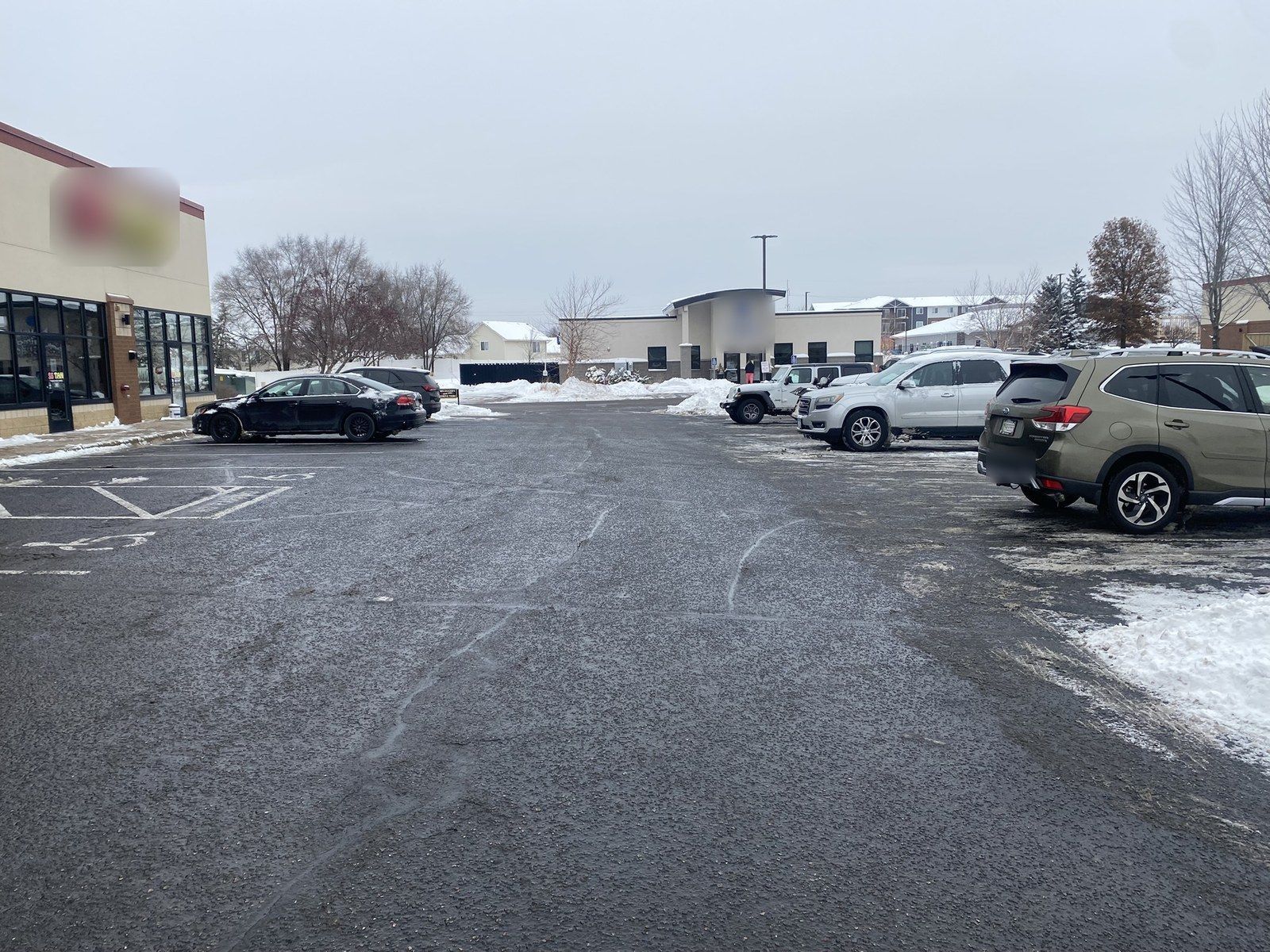 Cleared retail parking lot with cars parked near a row of shops