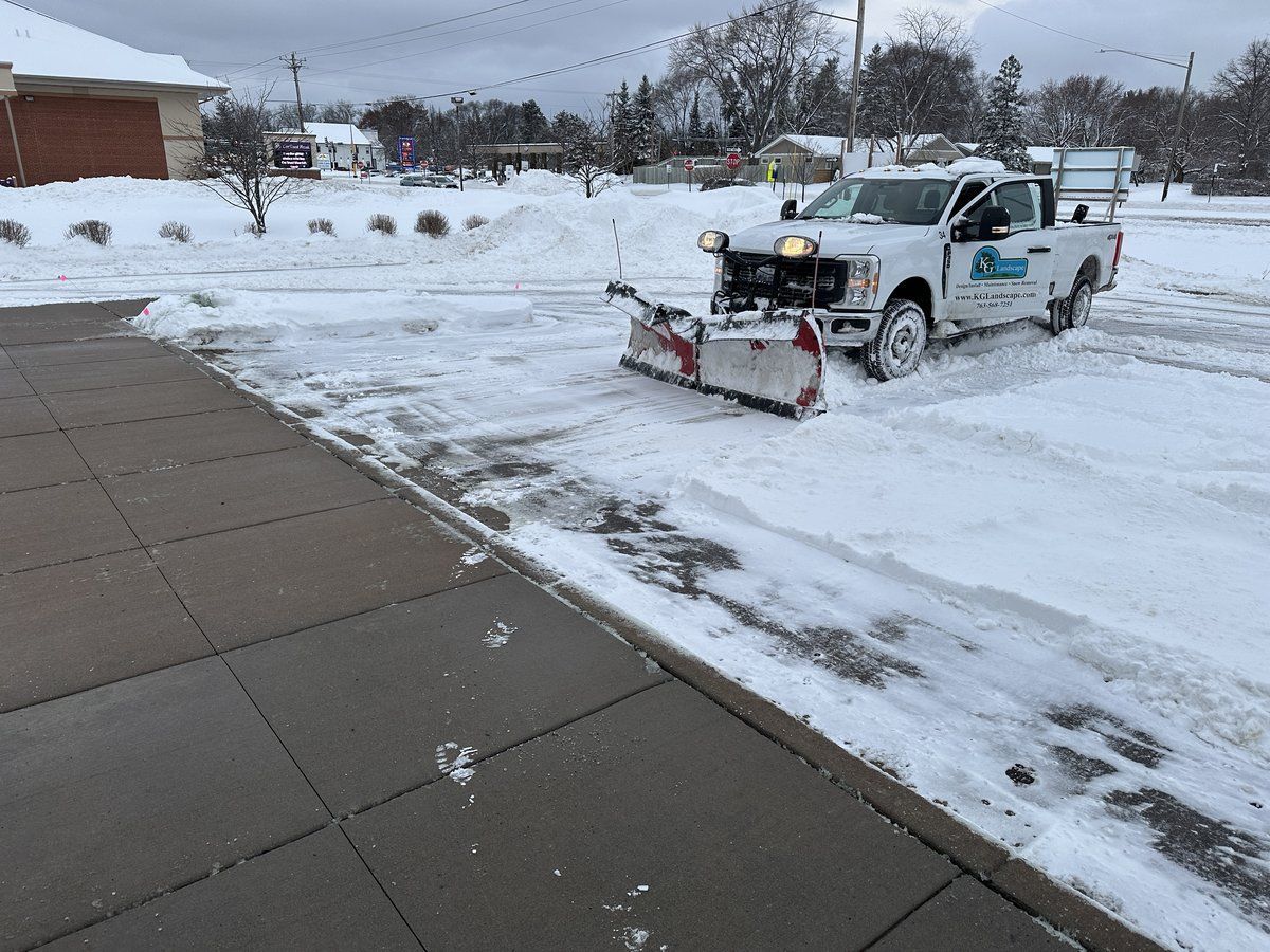 KG Landscape plow truck clearing an office parking lot next to a walk
