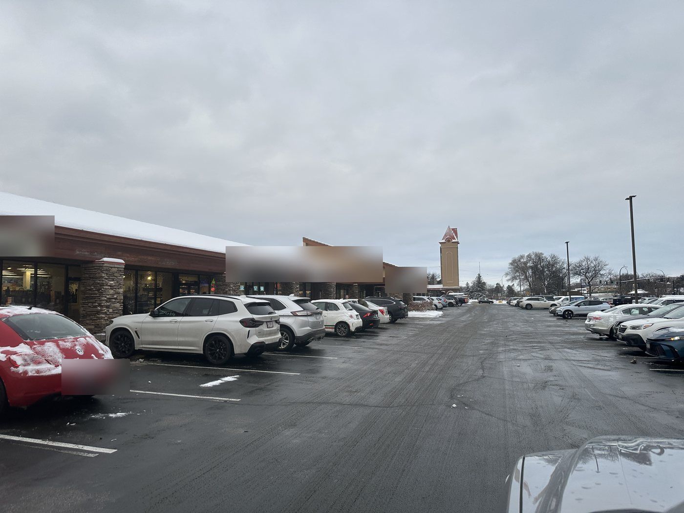 Strip center parking lot plowed to pavement with cars parked by the storefronts