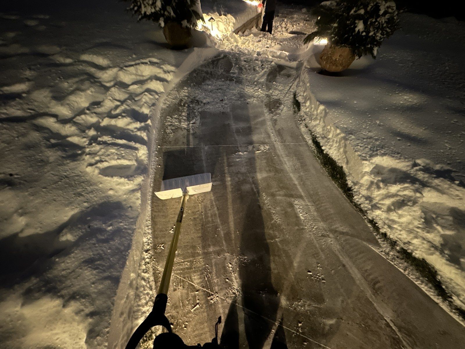 Snow shovel clearing a narrow front walk between snowbanks at night