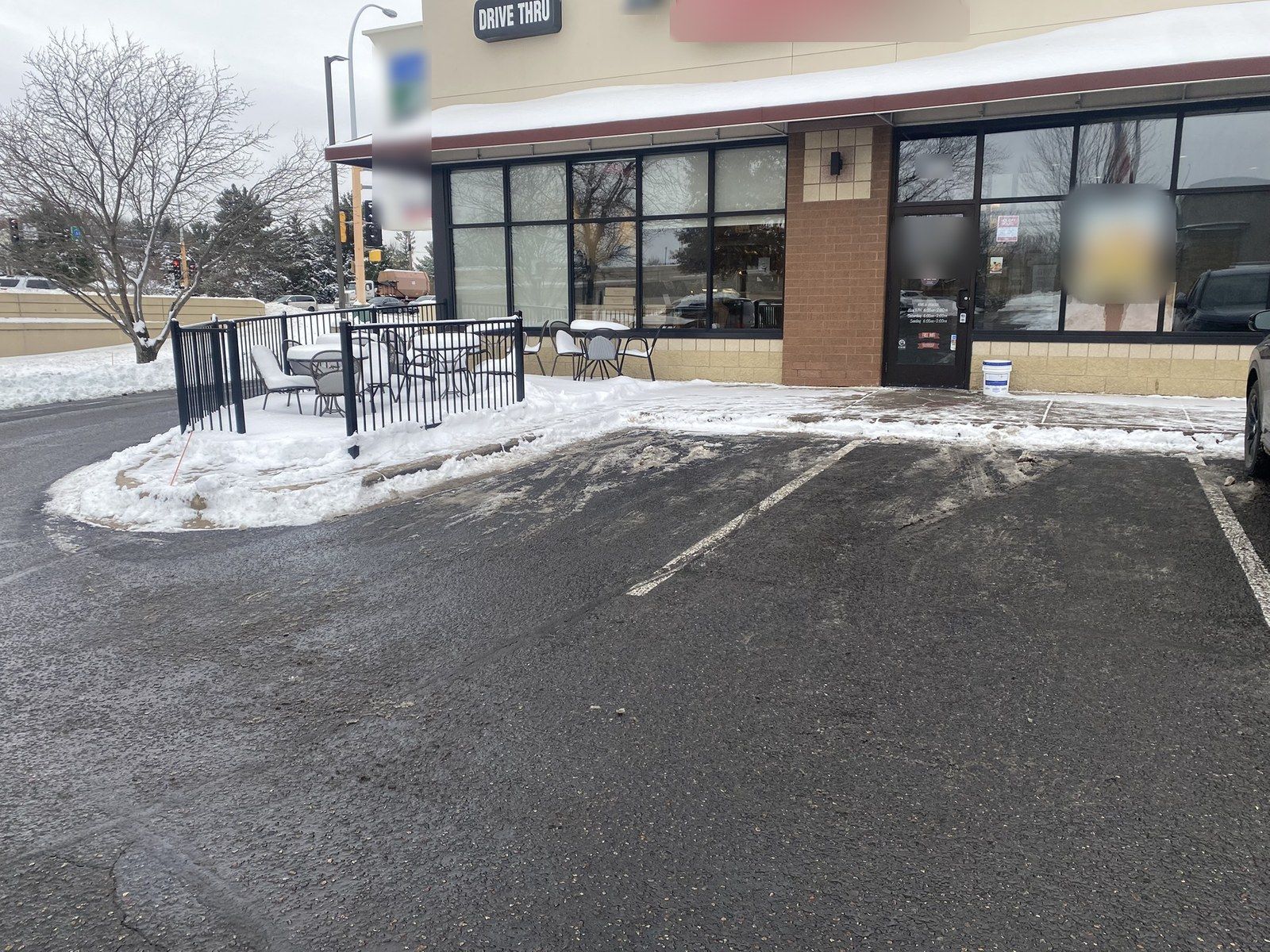 Shoveled storefront walk past a fenced patio with snow-covered tables and chairs