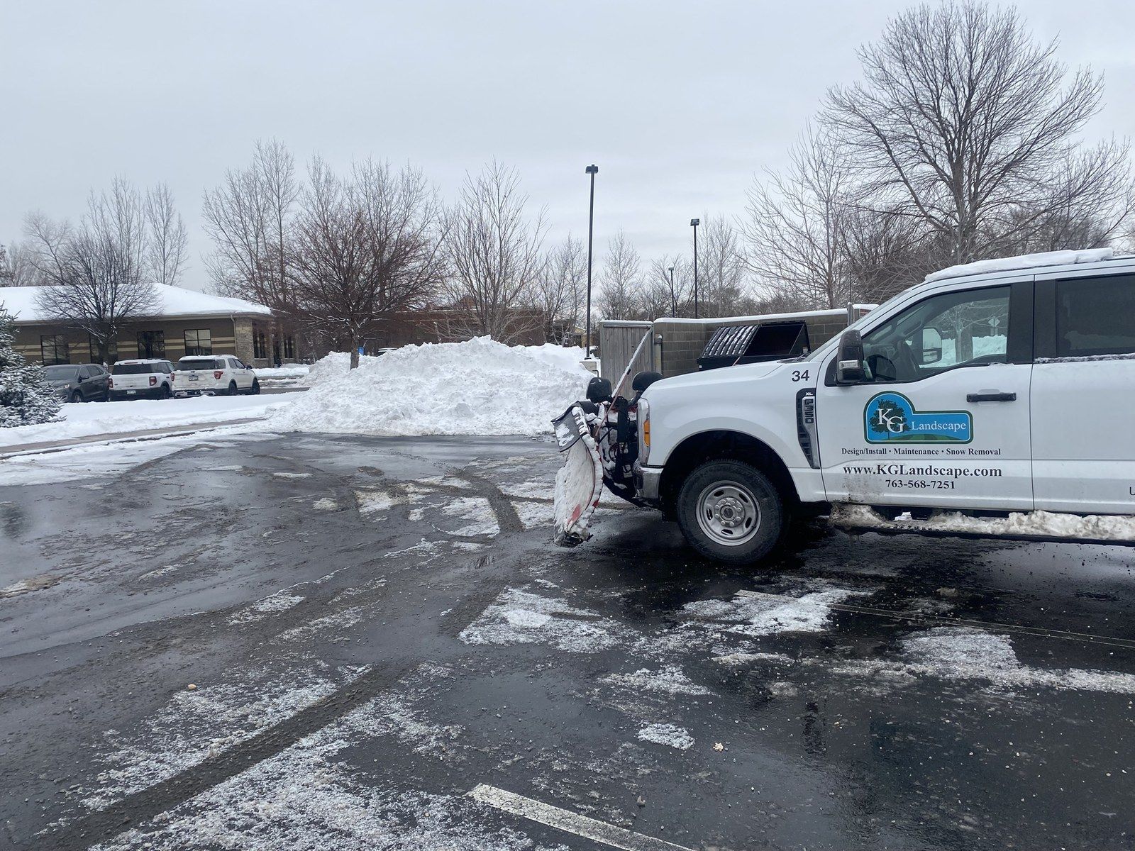 KG Landscape plow truck parked beside a tall snow pile in a commercial parking lot