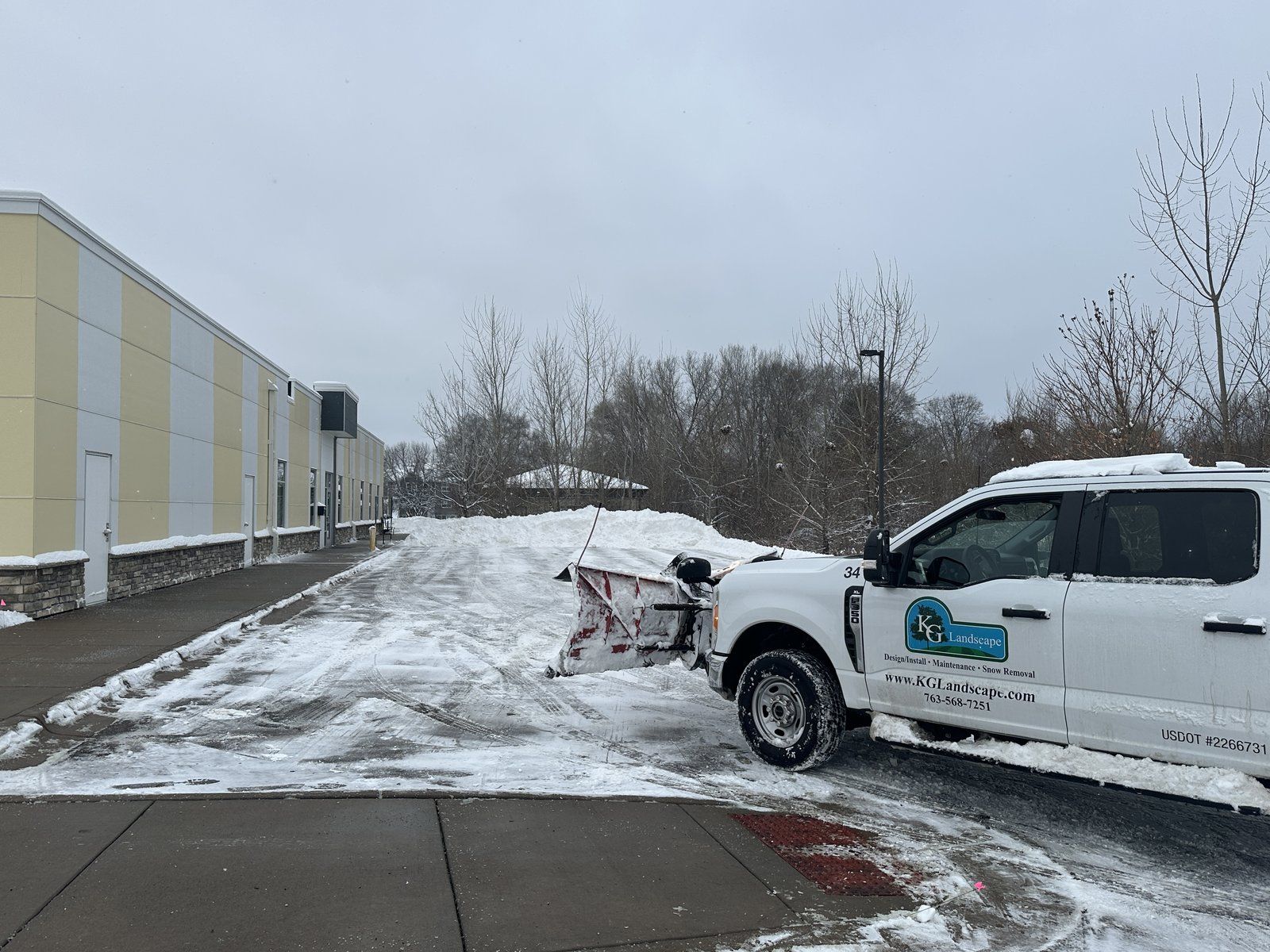 KG Landscape plow truck clearing snow along the walk at an office building