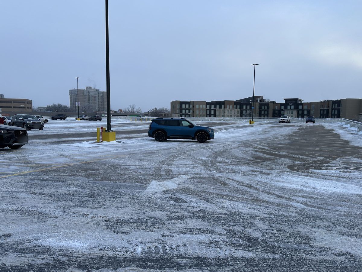 Plowed parking lot with multi-story buildings in the distance