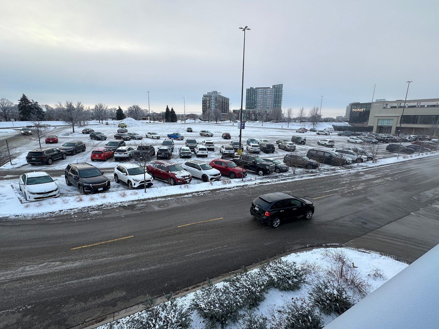 Large parking lot full of cars beside a plowed street