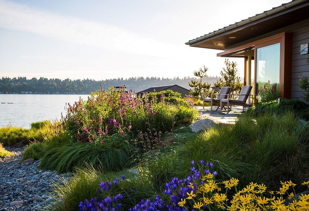 Lakeside home with a patio, surrounded by colorful flowers and greenery. Overlooking water and trees.