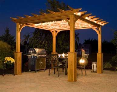 Wooden pergola with string lights over a patio dining area and a grill, at night.