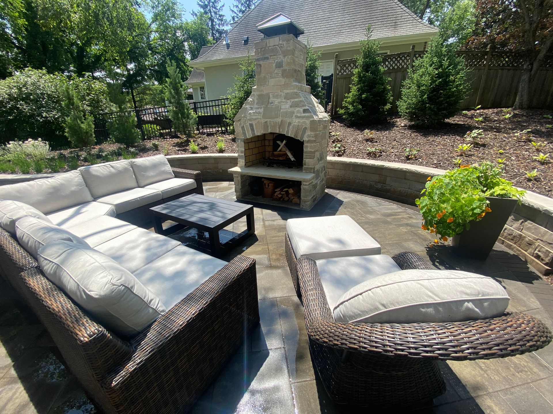 View from an L-shaped couch toward a custom stone fireplace on a Minnetonka paver patio with plantings and wall