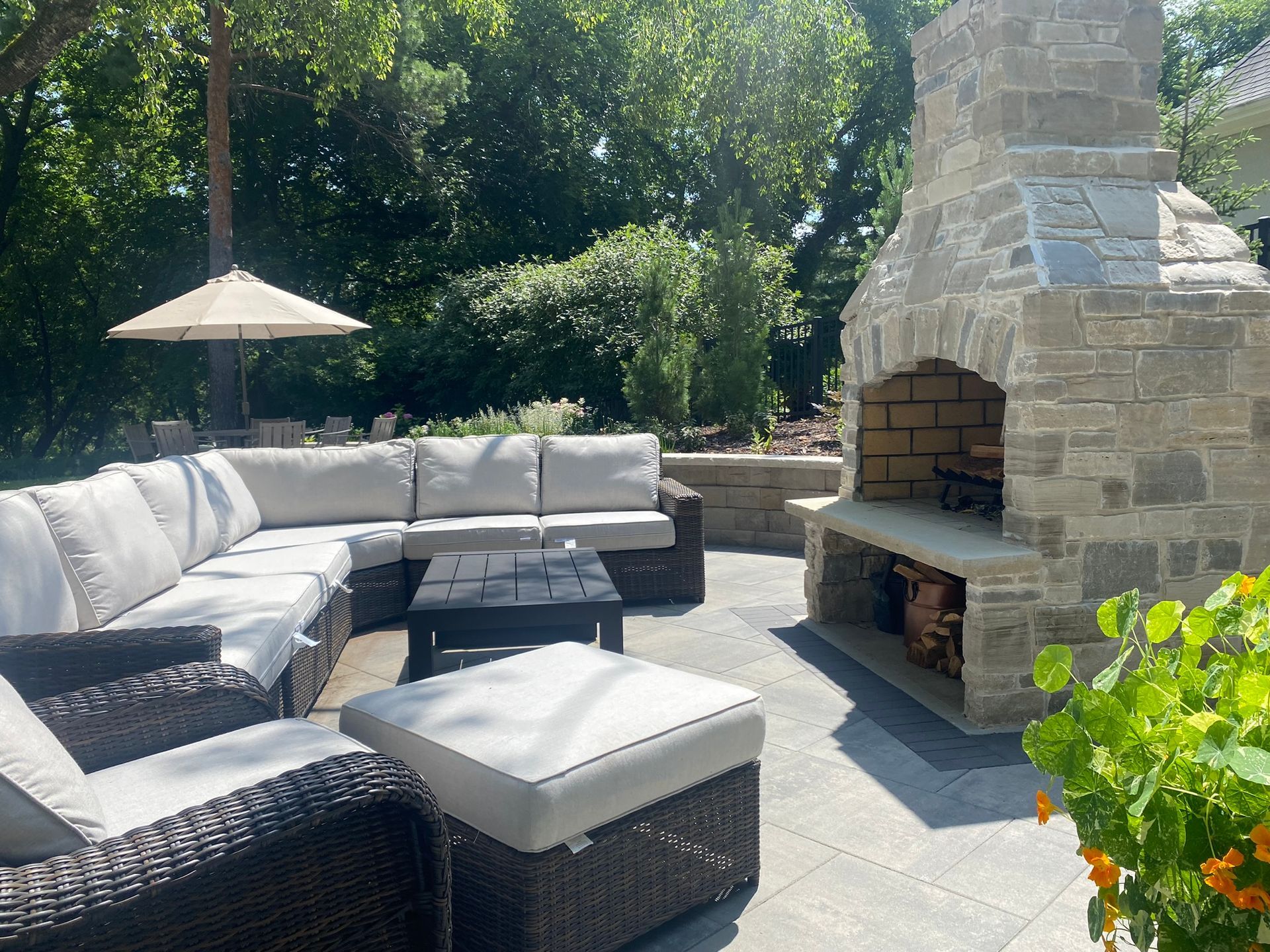 Gray paver patio in Minnetonka MN with outdoor fireplace, retaining wall, and wicker couch and chairs