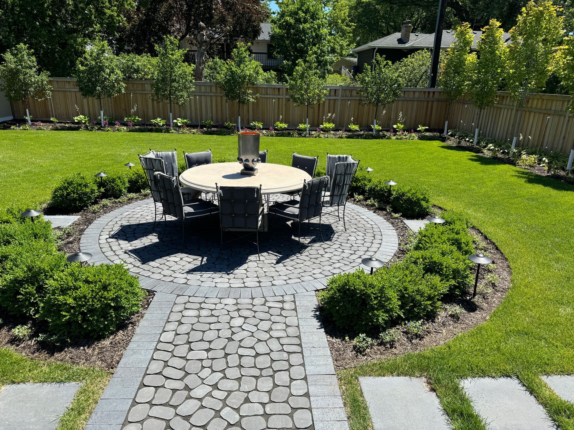 Edina MN backyard with privacy tree, cedar fence, plantings, dining table and chairs, and stepping stones