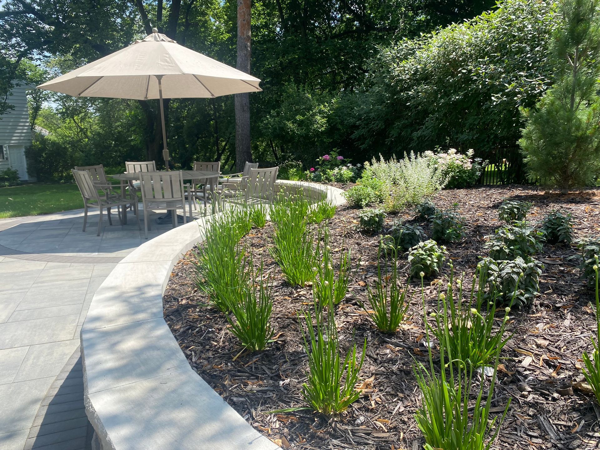 Curved paver patio in Minnetonka with capstone sitting wall, colorful perennials, and light gray stone fireplace