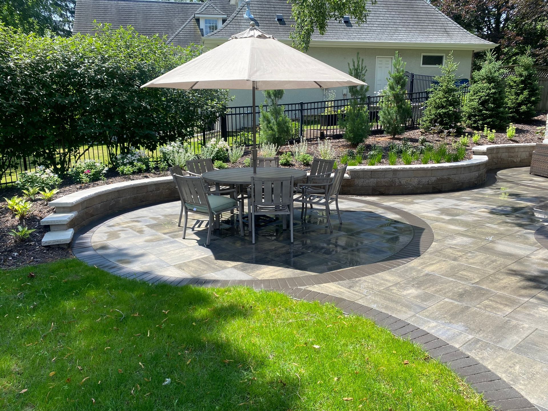 Dining table under an umbrella on a circular paver inlay, with limestone-capped sitting wall and perennials, Minnetonka