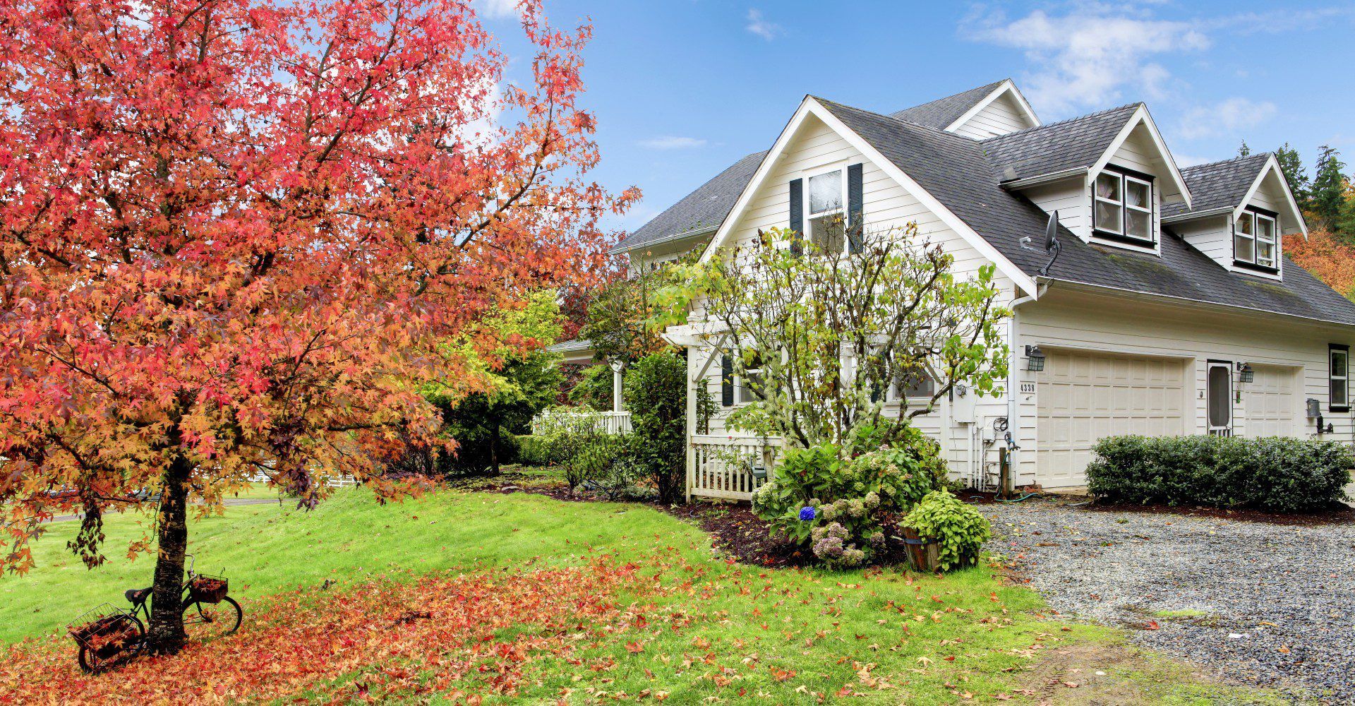 White house with a gray roof and attached garage next to a tree with red leaves in fall.