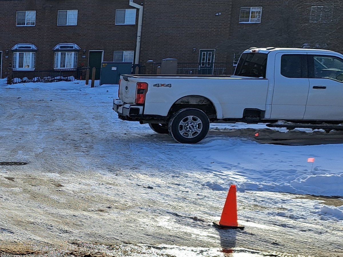 Plowed lot in front of an apartment building, with a pickup truck and an orange cone
