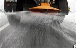 Snowplow spraying a substance on a snowy road, orange spreader, winter scene.