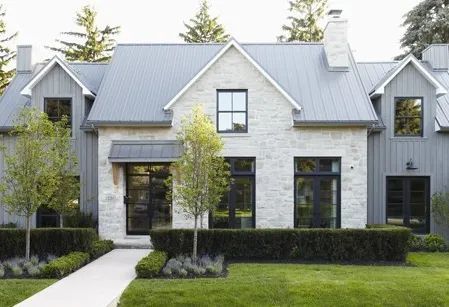Stone and gray house with black windows, metal roof, and manicured landscaping.