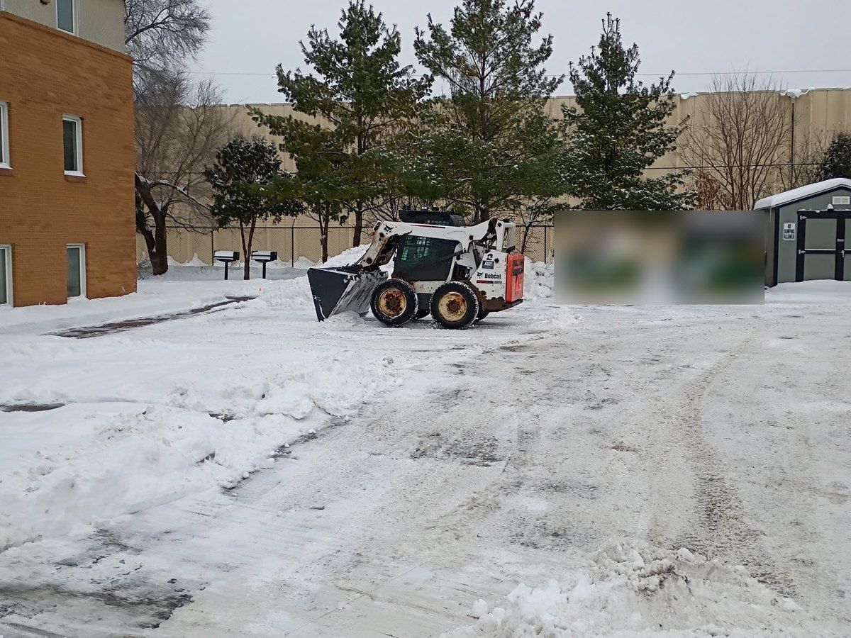 Skid loader working an open drive lane beside a building after a snowfall