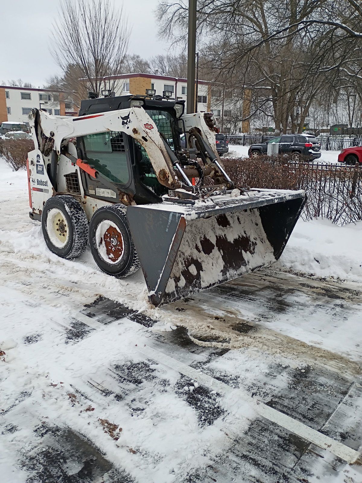 Skid loader clearing snow along the edge of a commercial parking lot