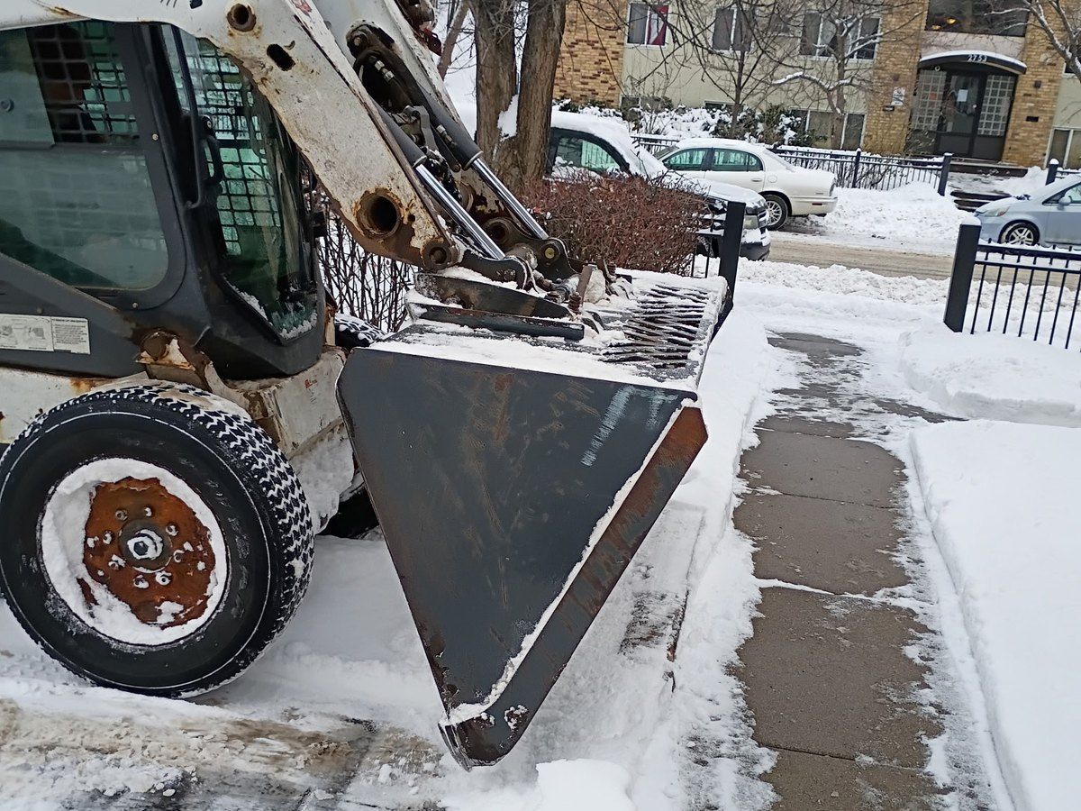 Skid loader bucket beside a cleared walk along a row of parked cars