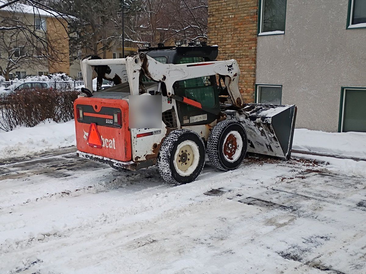 Skid loader parked by a building with the stalls behind it scraped to pavement