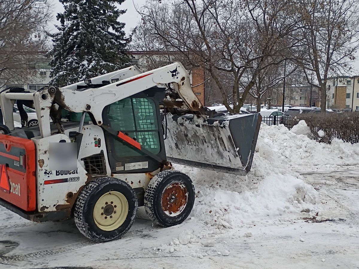 Skid loader pushing snow into a pile at the edge of a parking lot