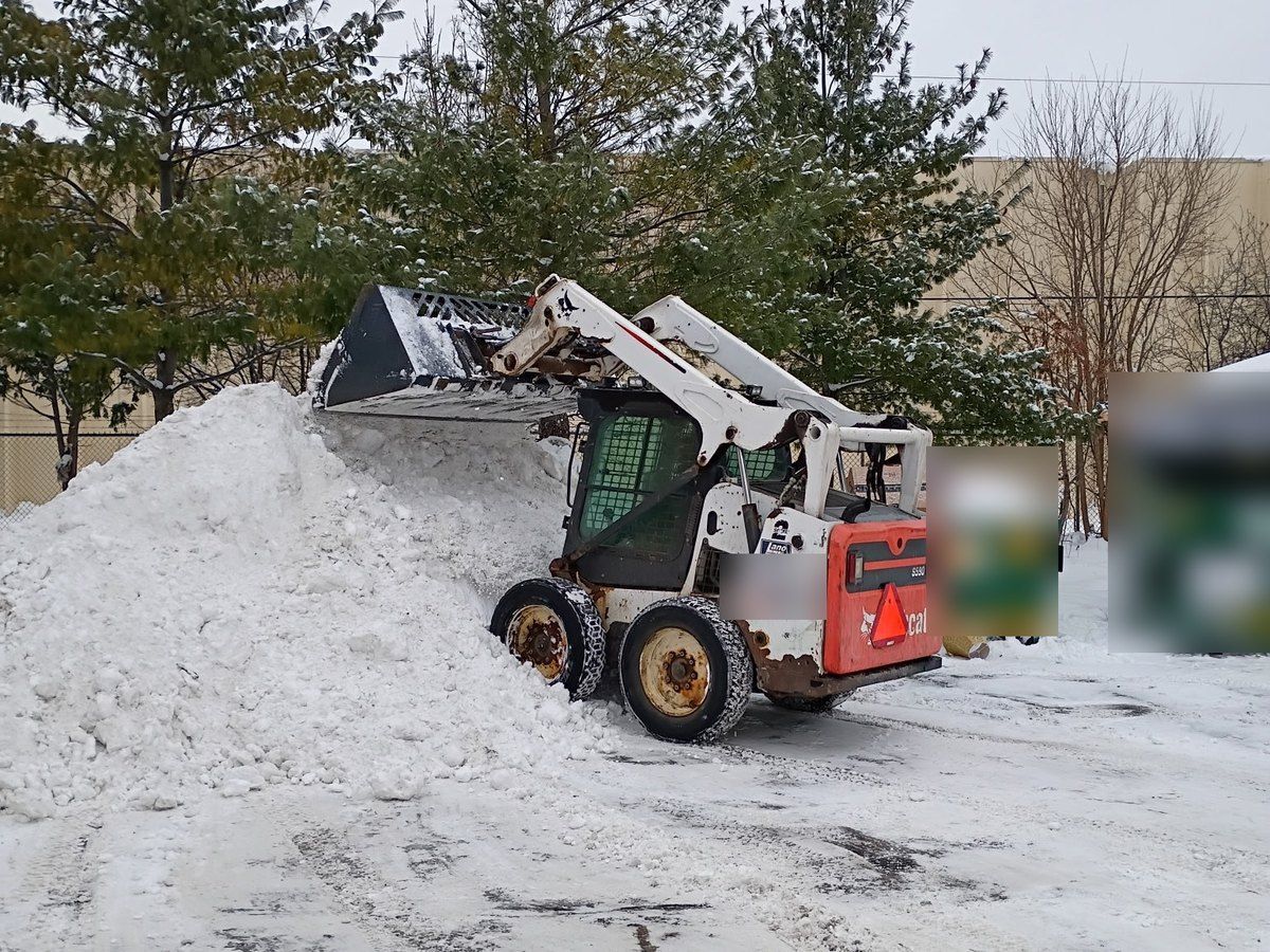 Skid loader pushing snow onto a tall pile beside two dumpsters
