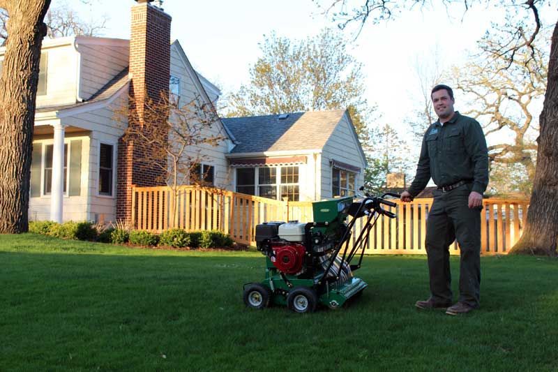 worker standing in lush green lawn with a slit seeder 