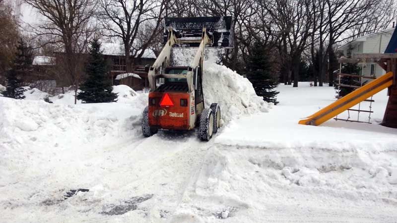 Orange Bobcat snowplow pushing snow, near a playground and trees.