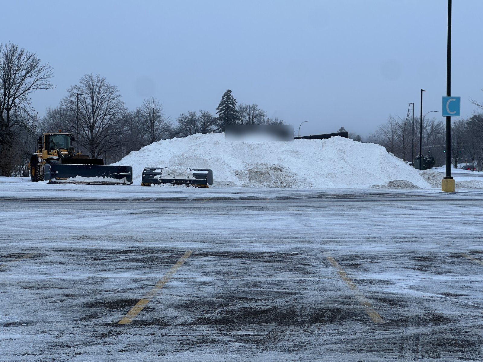 Large snow pile stacked at the edge of a cleared commercial parking lot