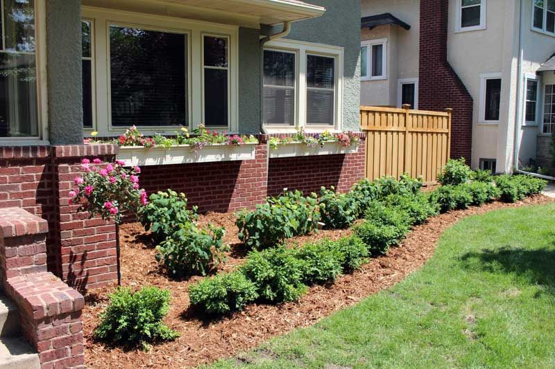 Well-maintained front yard with brick house, flower boxes, and neatly trimmed green bushes.