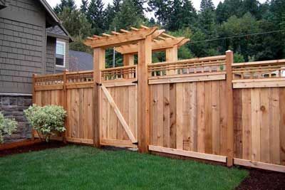 Wooden fence with gate and pergola over entrance; green lawn.