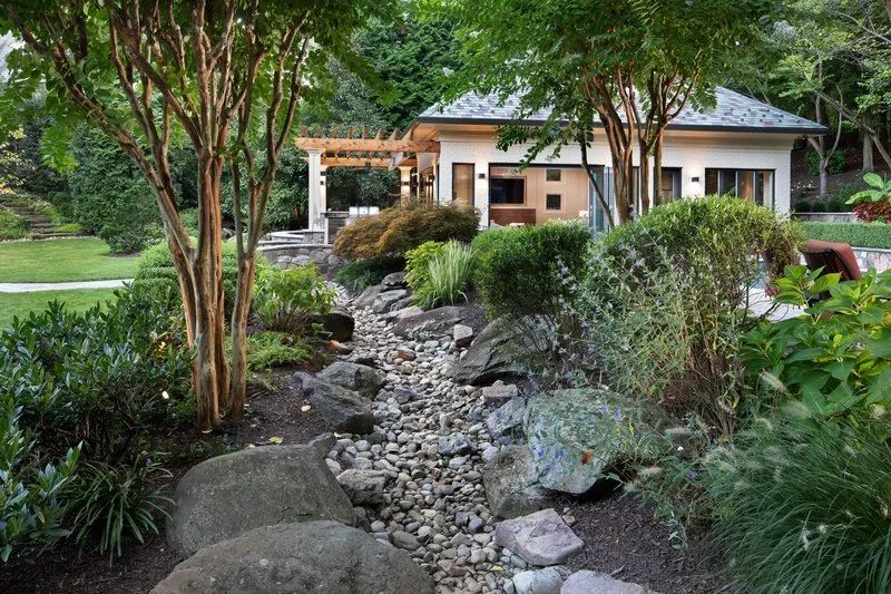 A house is surrounded by trees and rocks in a garden.