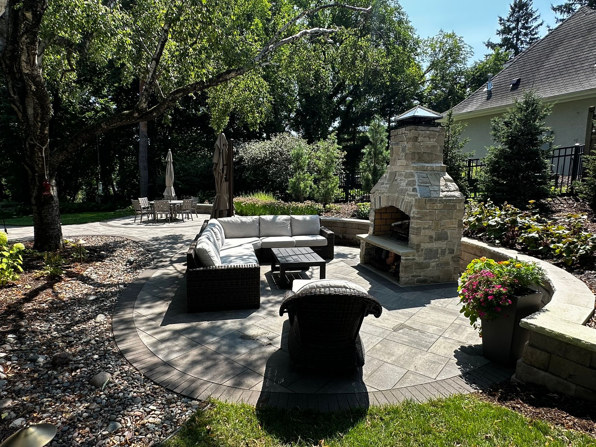 Great backyard paver patio with sitting wall and fireplace filled with nice plants and flowers in Minnetonka MN 