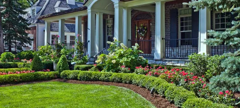 A large house with a lush green lawn and flowers in front of it.