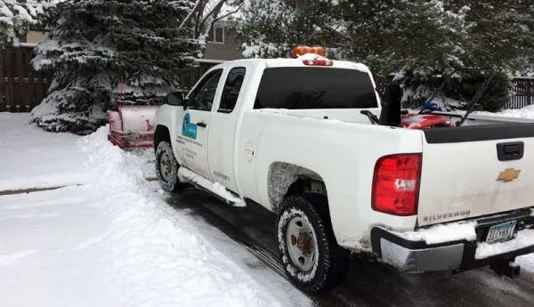 White pickup truck with snowplow clearing snow from a driveway.
