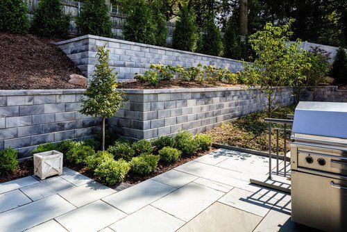 Stone retaining wall with plants in front of a house with a porch.